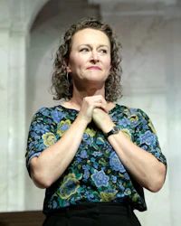 a woman with curly hair standing in front of a stage