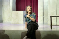 a woman is sitting on a stage in front of a curtain